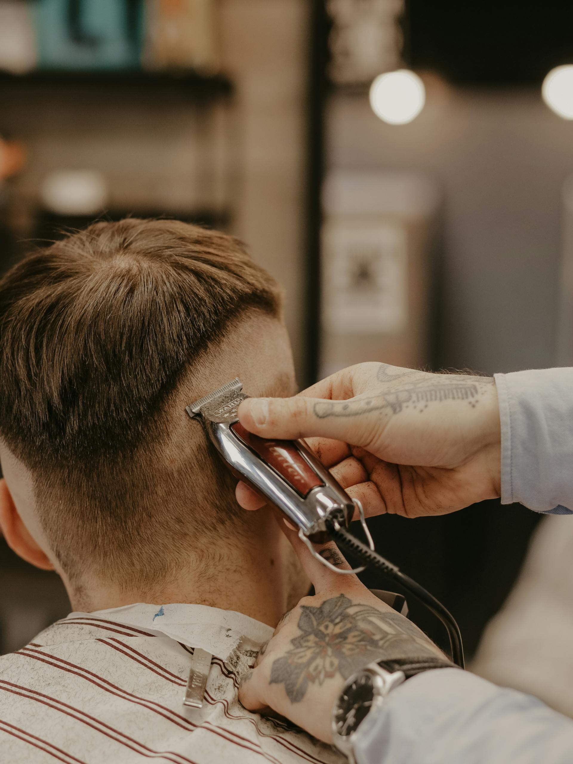 Tattooed barber working brass clippers on a fade